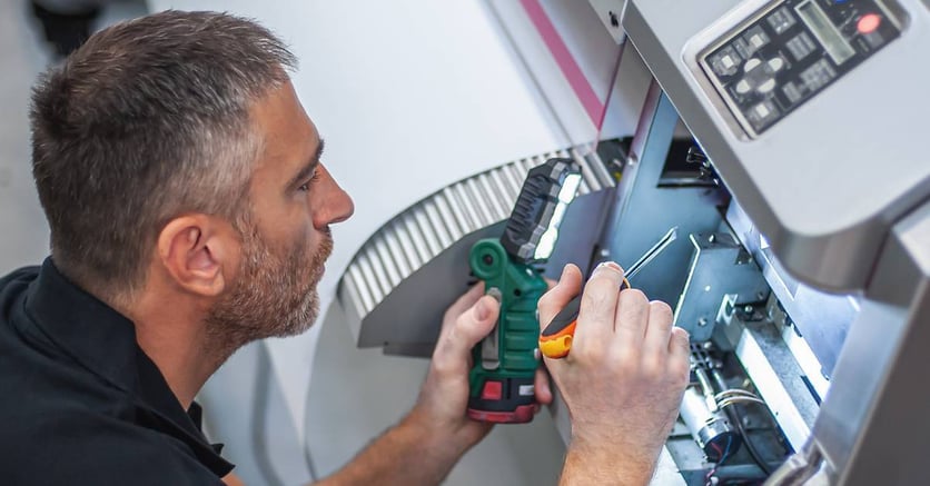 A male printer technician performing routine maintenance on a printer