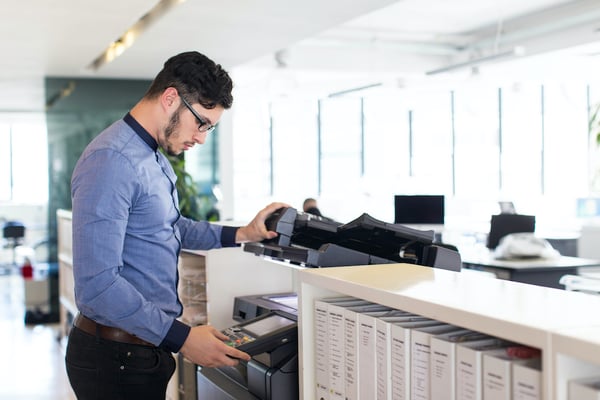 adult male office worker in a blue shirt using the office printer/scanner. 