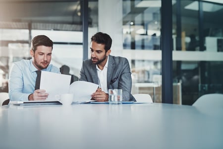Two businessmen discussing information at a table. 