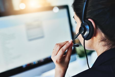 A help desk support staff member with a headset on looking at a computer screen