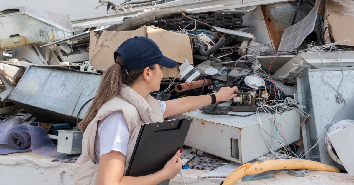A significant amount of IT waste is examined and documented by a female worker.