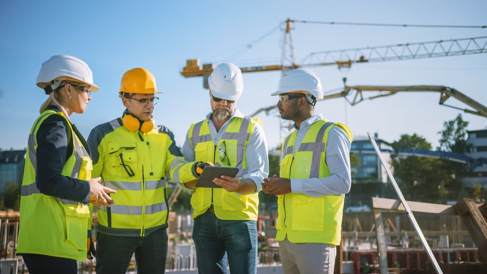 Team of construction workers consult a tablet on the job site. 