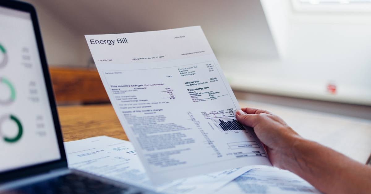 Someone looks at a utility bill next to a laptop showing analytics