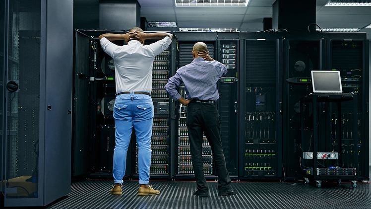 Two male IT professionals stuck in a break/fix cycle at their business troubleshoot an IT issue in their business's server room.